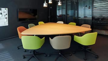 Una sala de conferencias con una gran mesa, seis sillas, un televisor de pantalla plana y lámparas colgantes.