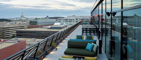 A rooftop terrace with outdoor seating, a view of the Capitol building, and a modern glass building in the background.