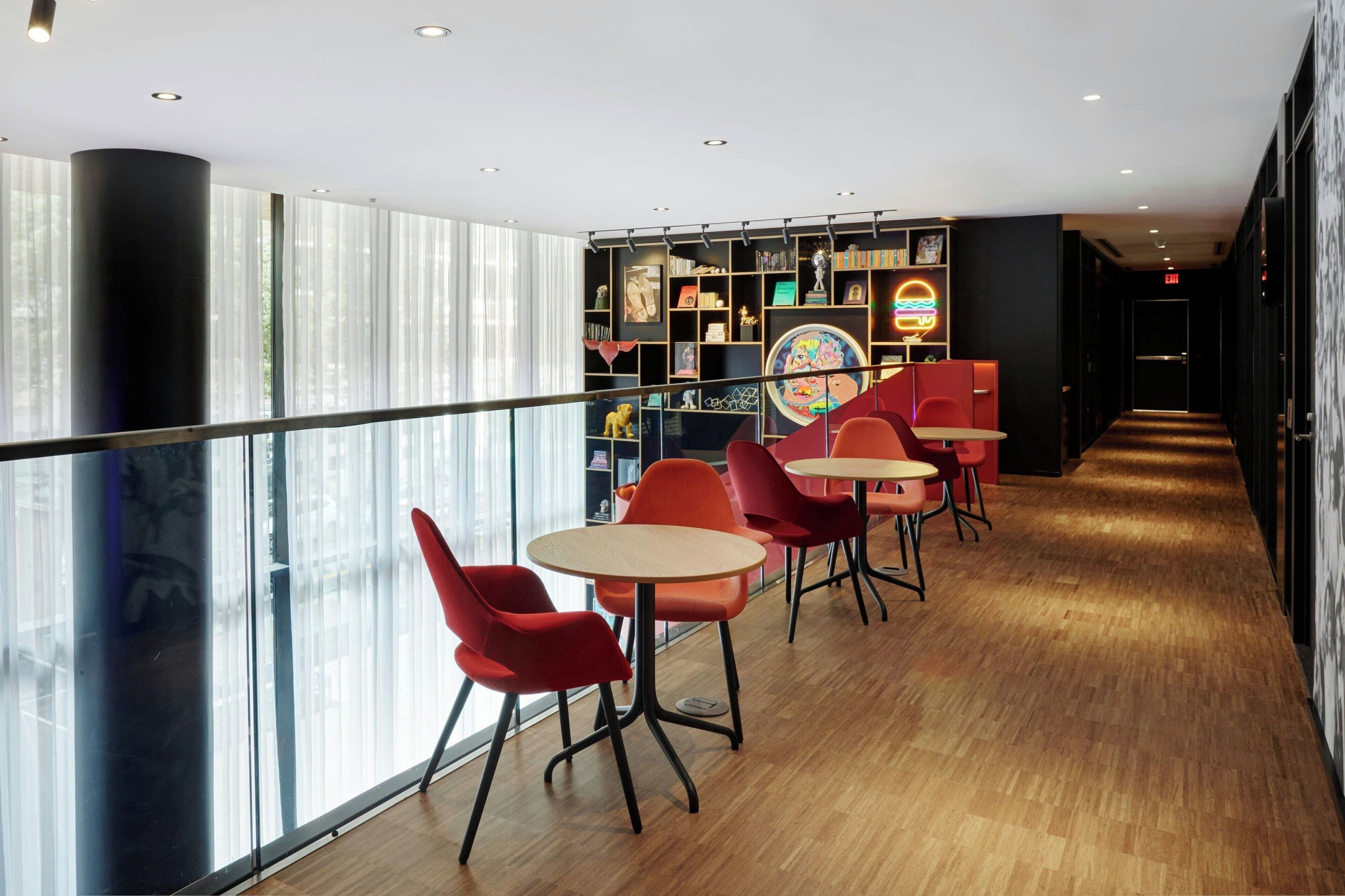 A modern interior with red chairs and tables, a glass railing, and a bookshelf with various items.