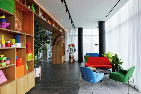 A modern interior with a wooden bookshelf, colorful chairs, and a large window.