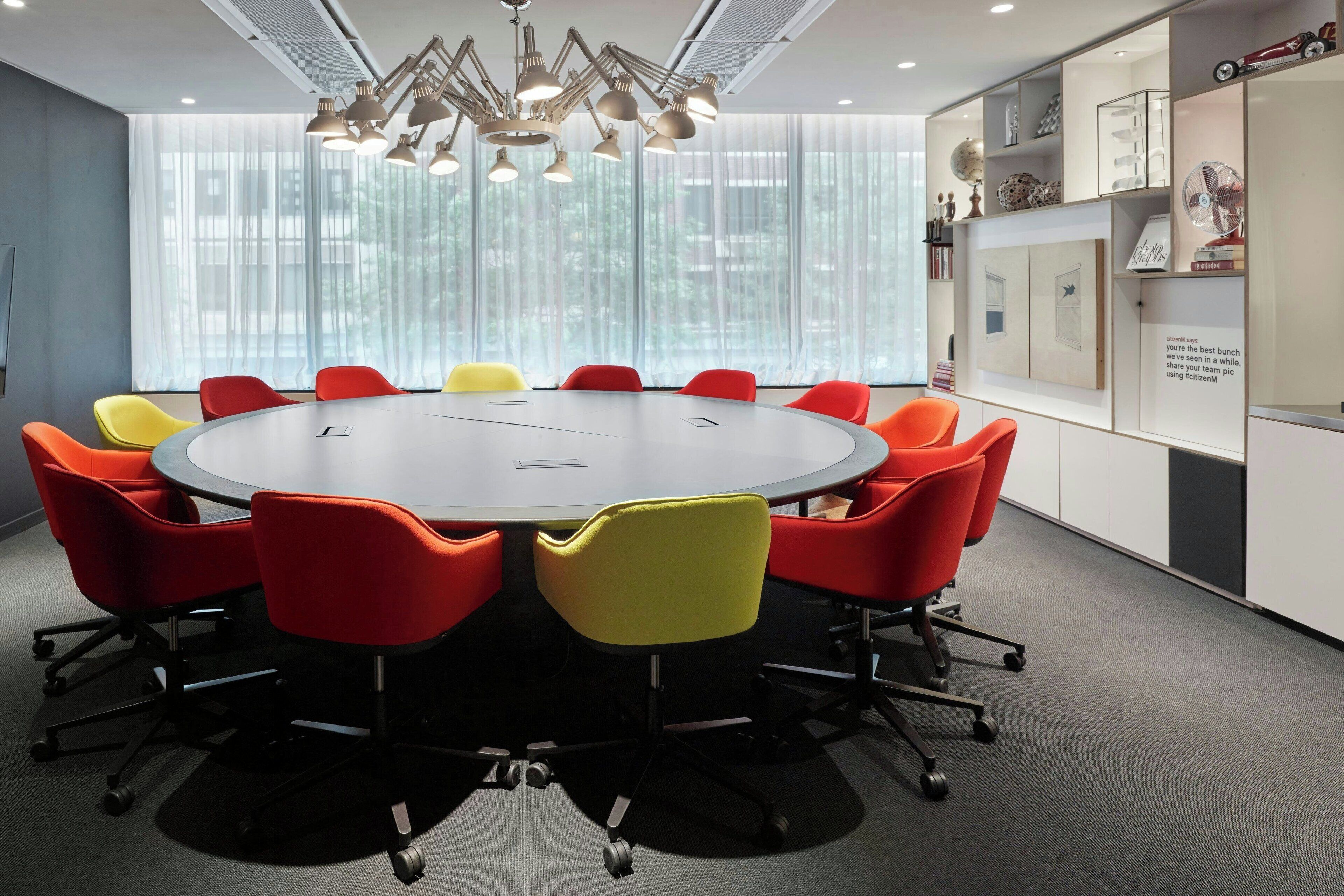 A conference room with a round table, colorful chairs, and a modern chandelier.