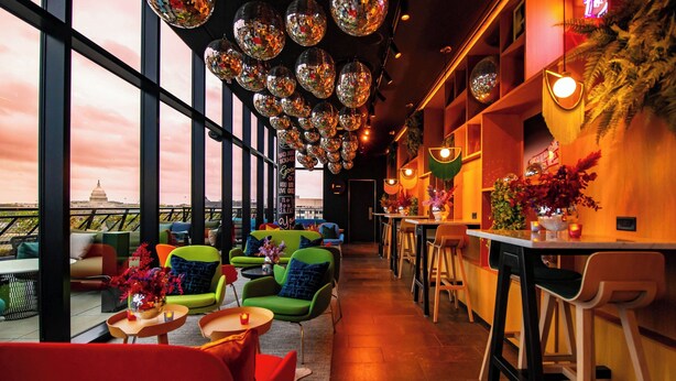 Eine moderne Bar mit lebendigen grünen und roten Stühlen, einer langen Theke und Blick auf das Kapitolgebäude.