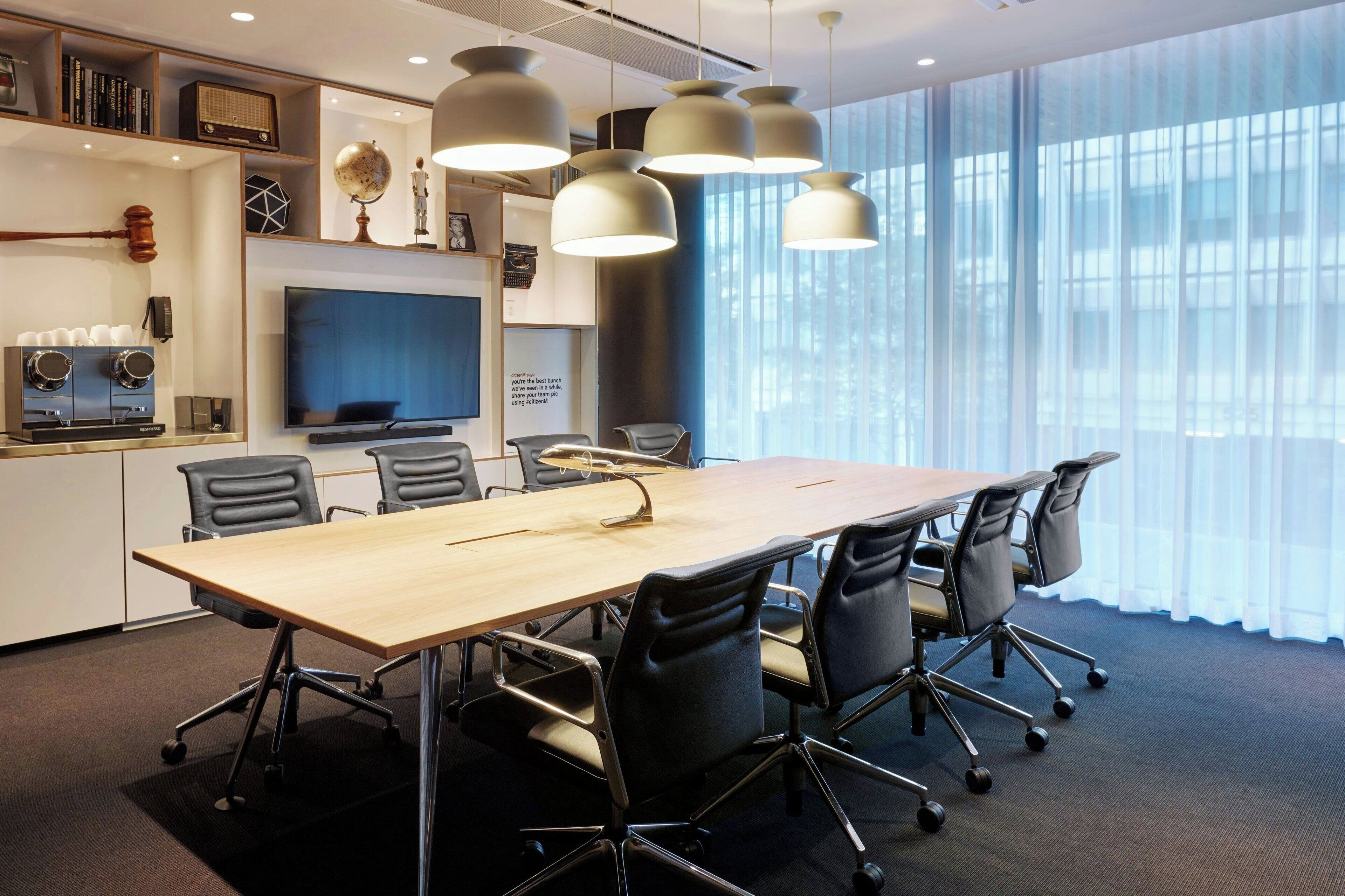 A conference room with a long table, black chairs, a television, and pendant lights.