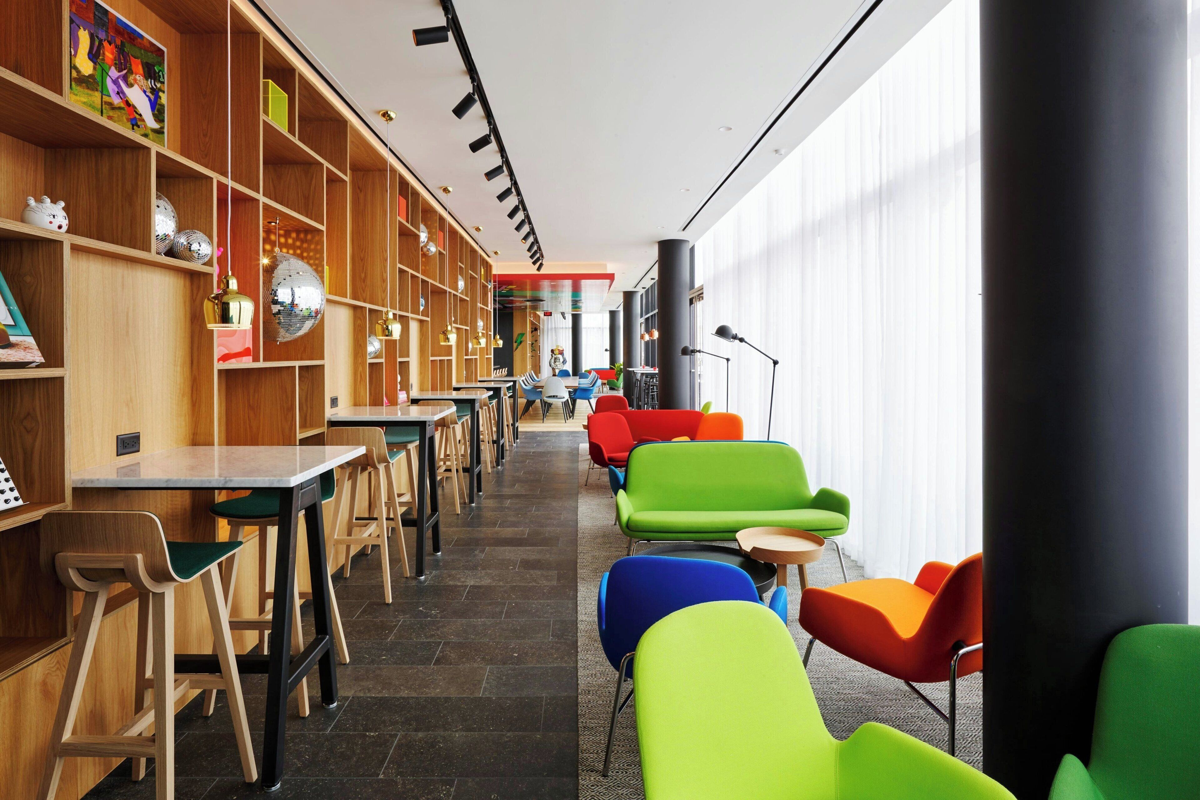 A modern library with wooden bookshelves, colorful chairs, and a long table.
