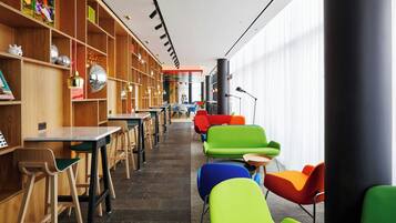 Uma biblioteca moderna com estantes de madeira, cadeiras coloridas e uma mesa comprida.