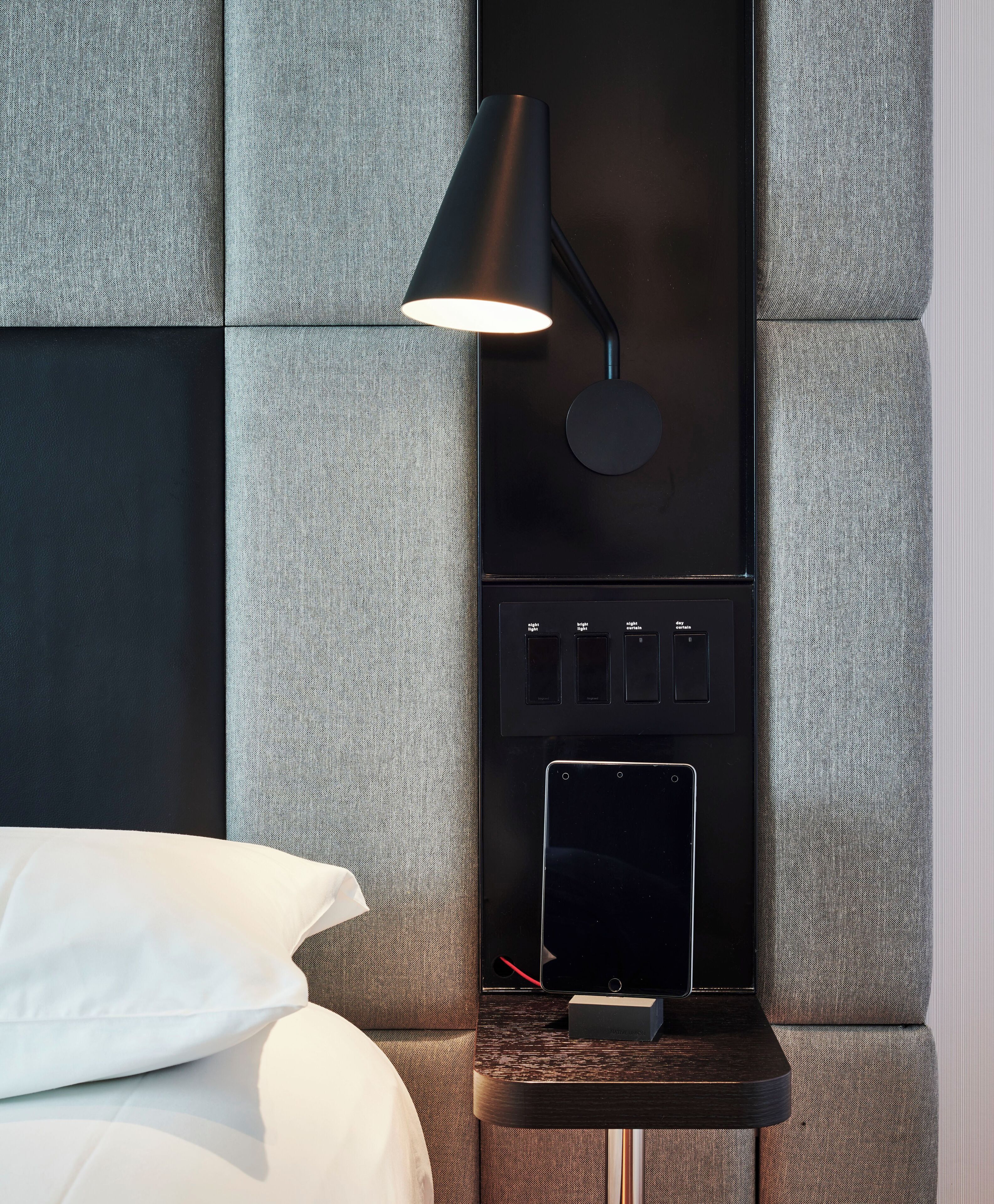 Une chambre d’hôtel moderne équipée d’un lit, d’une table de chevet avec une lampe et d’un panneau de commande.