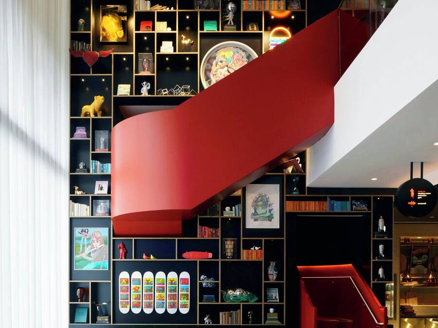 A modern interior with a spiral staircase, a bookshelf filled with books and decorative items, and a seating area with green chairs and a table.