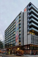 A modern hotel with a large glass facade, multiple balconies, and a prominent entrance with illuminated signage.