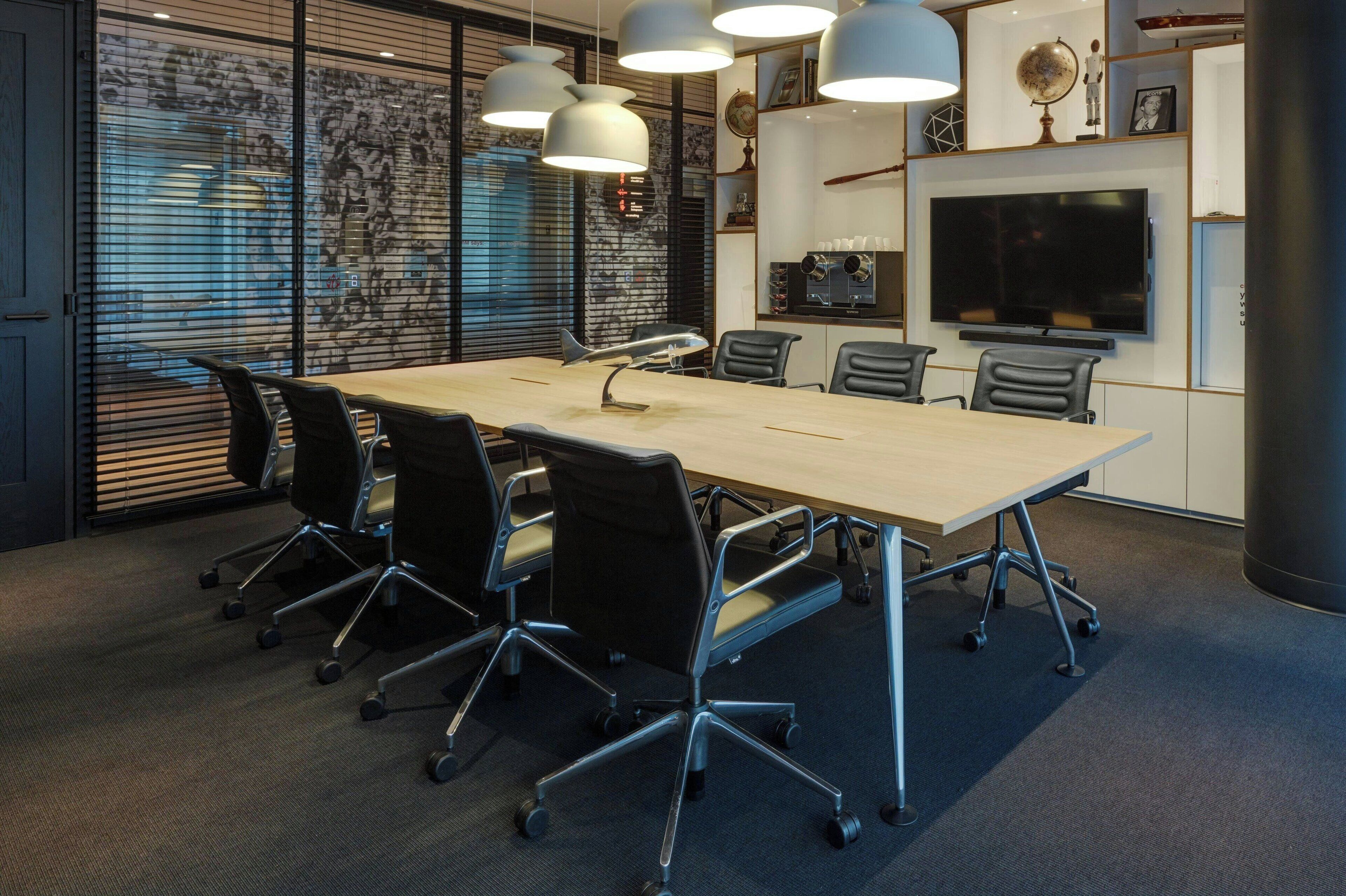 A conference room with a long table, six chairs, and three pendant lights.
