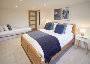 Un dormitorio con una cama de madera, ropa de cama blanca, un plaid azul oscuro y una mesita de noche blanca con una lámpara.