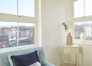 Relax in this serene room with a view of the residential area through large windows, featuring a light blue armchair and a small bedside table.