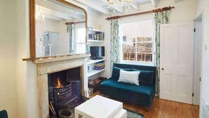 Una sala de estar acogedora con chimenea, un sofá color esmeralda, una mesa de centro blanca y un espejo grande.