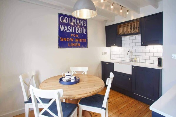 Une cuisine moderne avec des meubles de couleur sombre, un pare-feu en carreaux blancs et une table à manger en bois avec des chaises blanches.