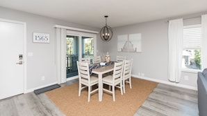 A dining area with a table and chairs, a chandelier, a door with a number, and a view through a window.