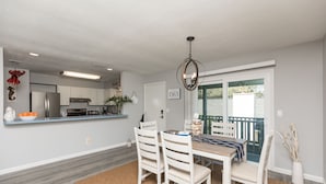 A modern kitchen with white cabinets, a stainless steel refrigerator, and a dining area with a wooden table and white chairs.
