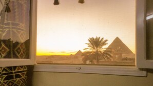 Une fenêtre donnant sur des pyramides et un palmier au coucher du soleil.