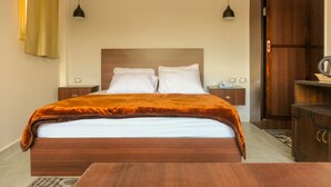 Une chambre d’hôtel avec un lit en bois, deux tables de chevet, une petite table, une armoire et deux lampes suspendues.