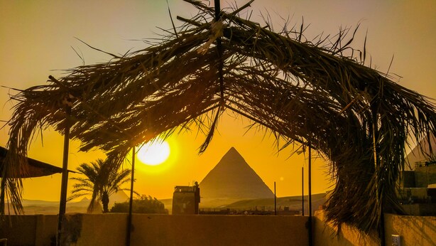 Une structure au toit de chaume offrant une vue sur la pyramide au coucher du soleil.