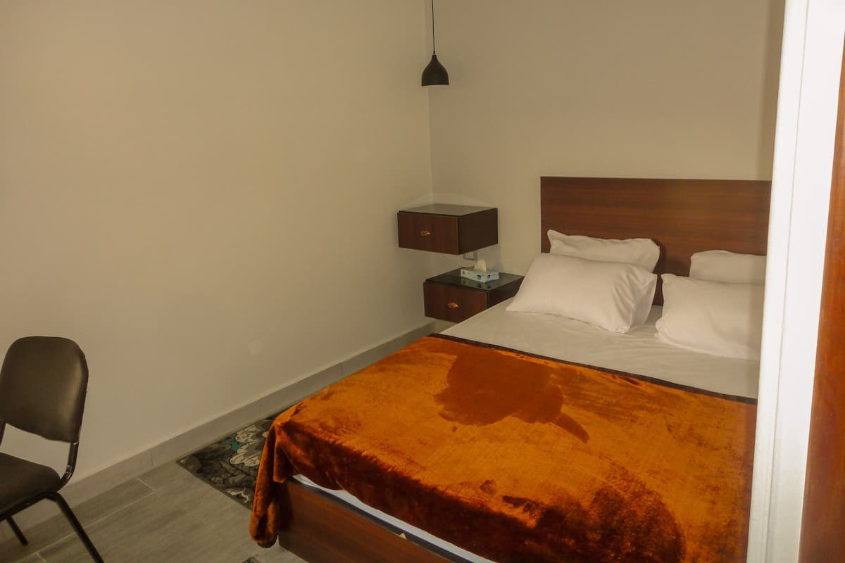 A hotel room with a bed, a nightstand, a chair, and a hanging light fixture.