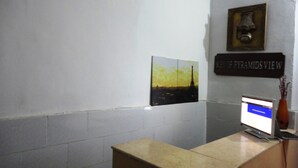 Un comptoir d’accueil avec un écran d’ordinateur, une photo encadrée de la Tour Eiffel et une pancarte indiquant « VUE SUR LES PYRAMIDES ».
