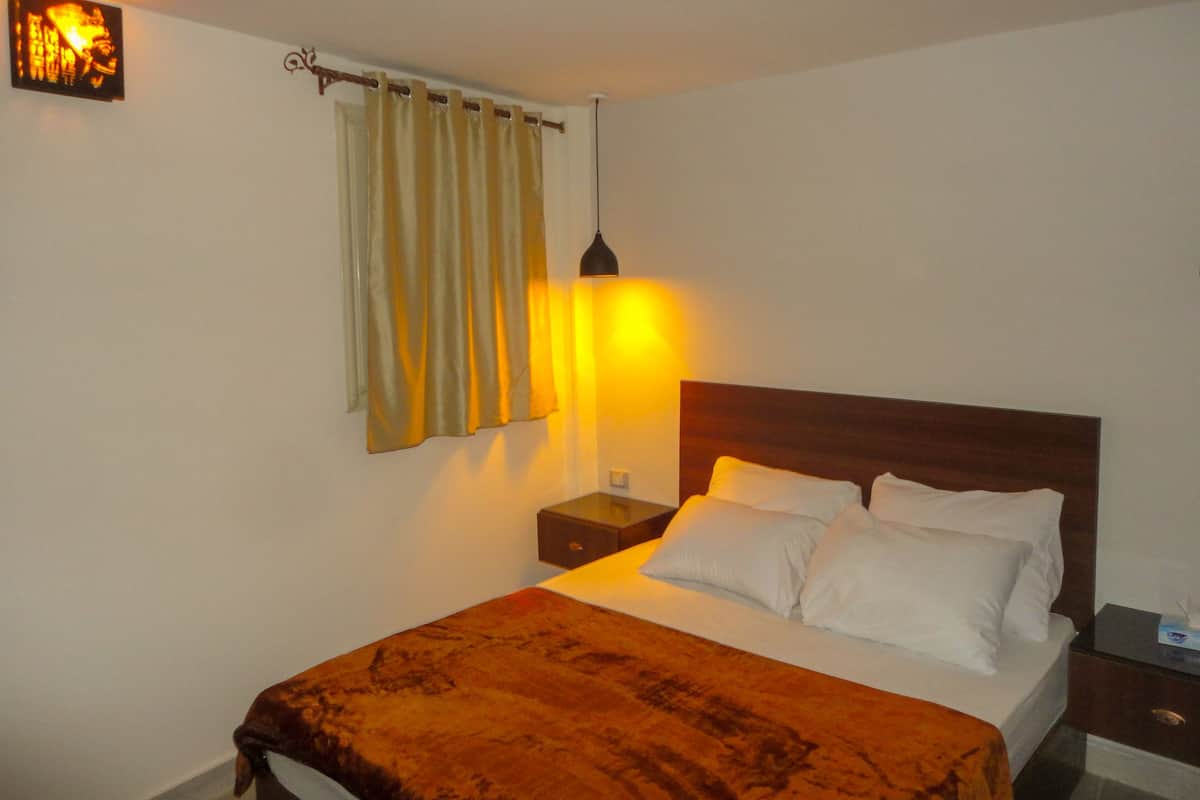 A neatly made bed with a brown blanket, a bedside lamp, and a wall-mounted picture.