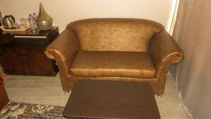 Un canapé en cuir marron et un pouf assorti dans un salon doté d’un sol carrelé et d’un tapis à motifs.