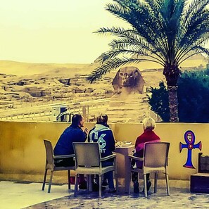 Un grupo de personas cenando en una mesa al aire libre con vistas a una gran estatua del esfinge egipcio.