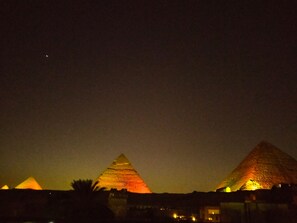 Vista nocturna de las pirámides iluminadas, con cielo despejado y una luna distante.
