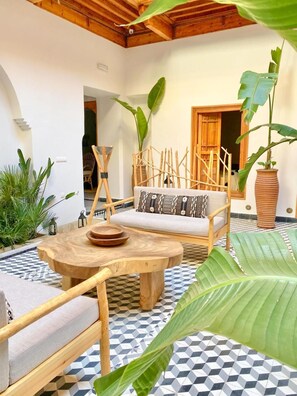 Un espace de détente extérieur accueillant, avec une table ronde en bois, des chaises rembourrées et un canapé agrémenté de coussins à motifs.