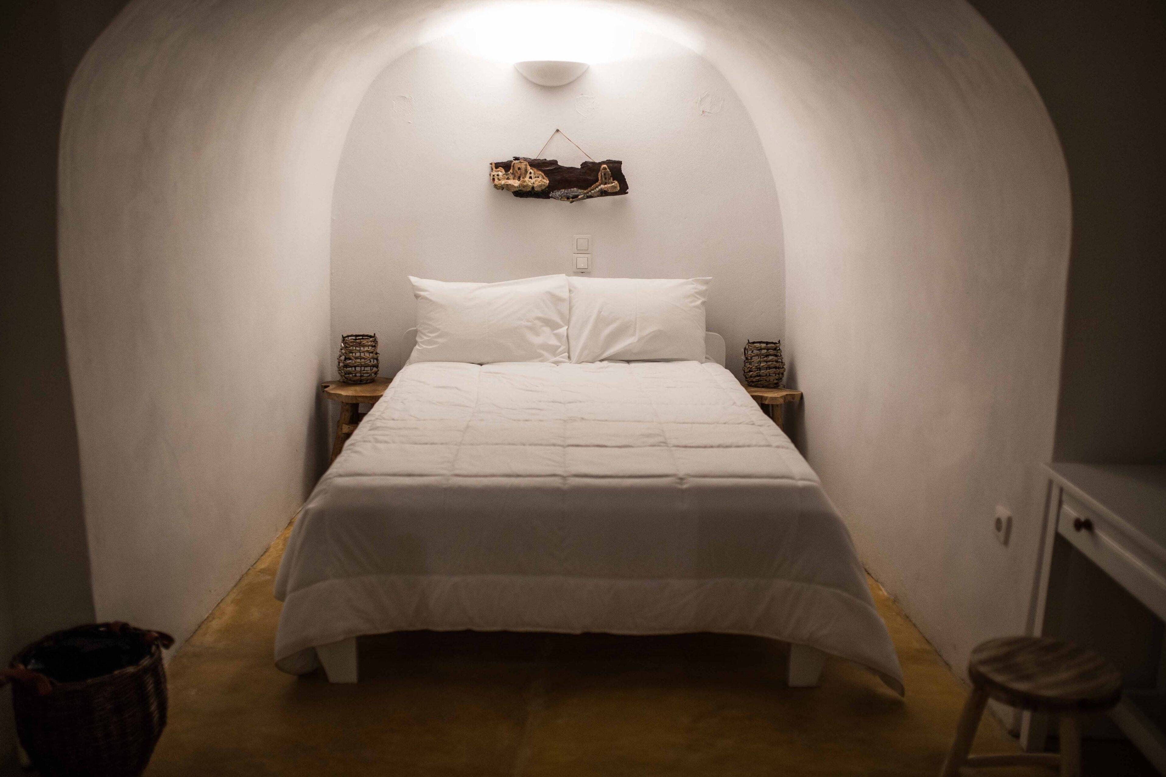 A cozy, white-walled bedroom with a single bed, a hanging light fixture, and a small wooden stool.