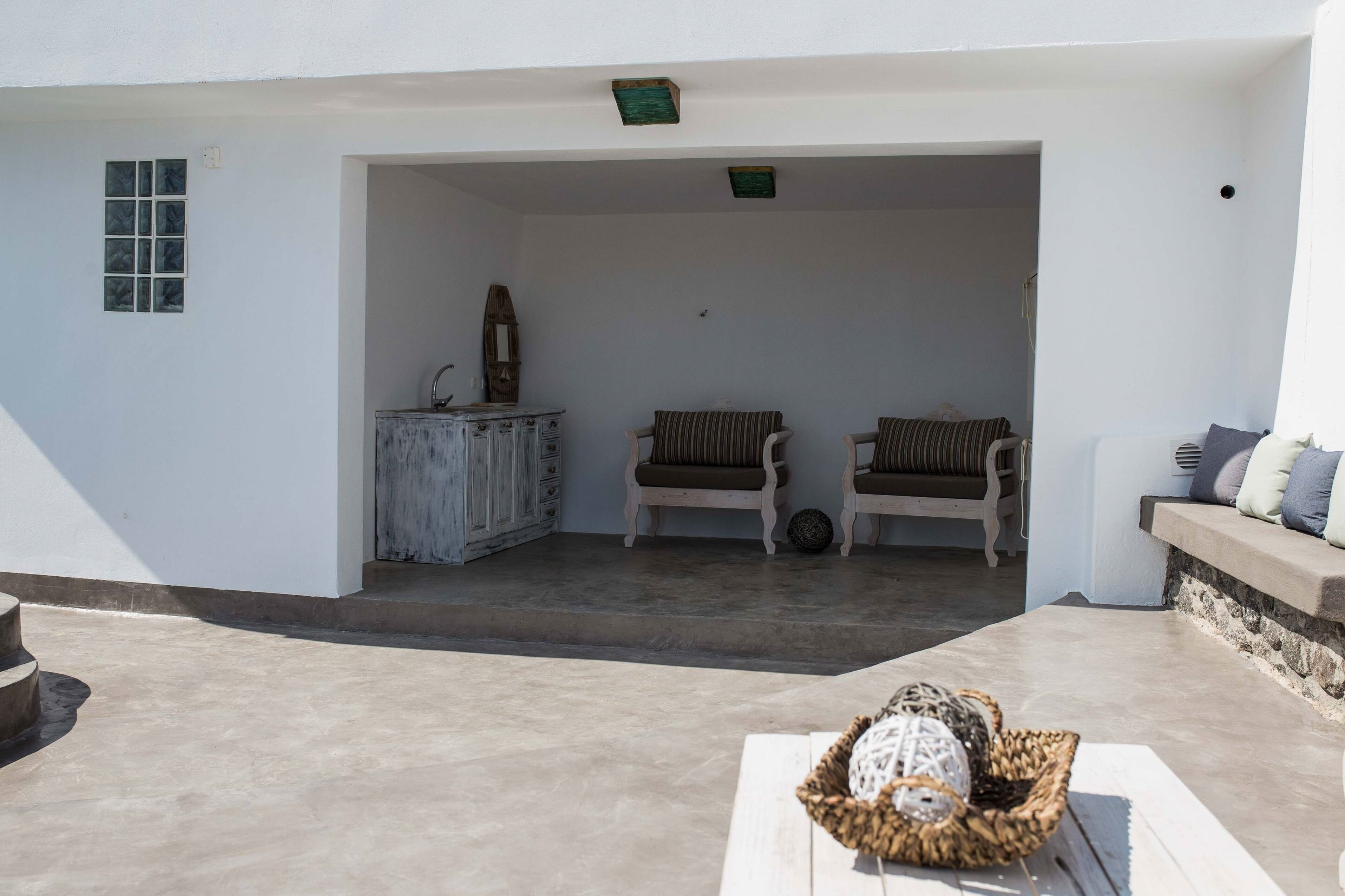 An open-plan living area with a white exterior, two cushioned chairs, a small cabinet, and a wicker basket with balls.