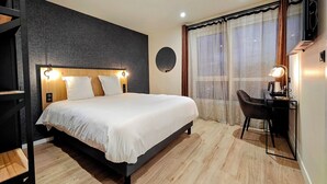 Une chambre d’hôtel moderne, dotée d’un grand lit, d’un bureau avec une chaise et d’un téléviseur fixé au mur.