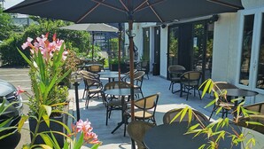 Un espace extérieur aménagé en terrasse, avec des tables et des chaises, entouré de plantes en pot et d’un grand parasol.