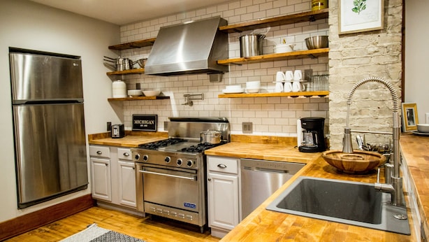 Cozinha moderna com eletrodomésticos de aço inoxidável, bancadas de madeira e painel de azulejos brancos.