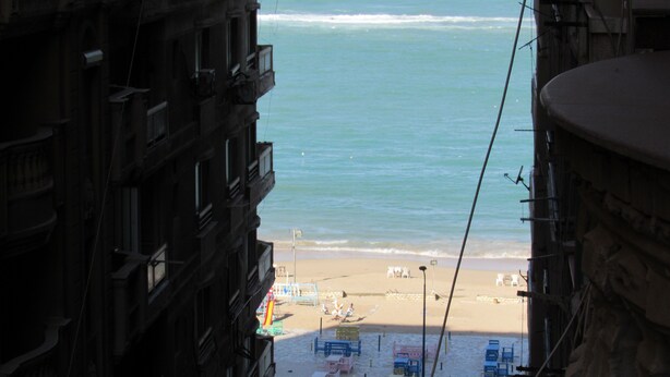 Vista de una playa con una fila de sillas y sombrillas coloridas, una orilla arenosa y el océano.
