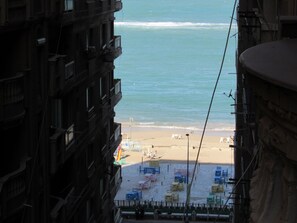 Une vue sur une plage avec une rangée de chaises de plage et de parasols aux couleurs vives, un rivage sablonneux et l’océan.