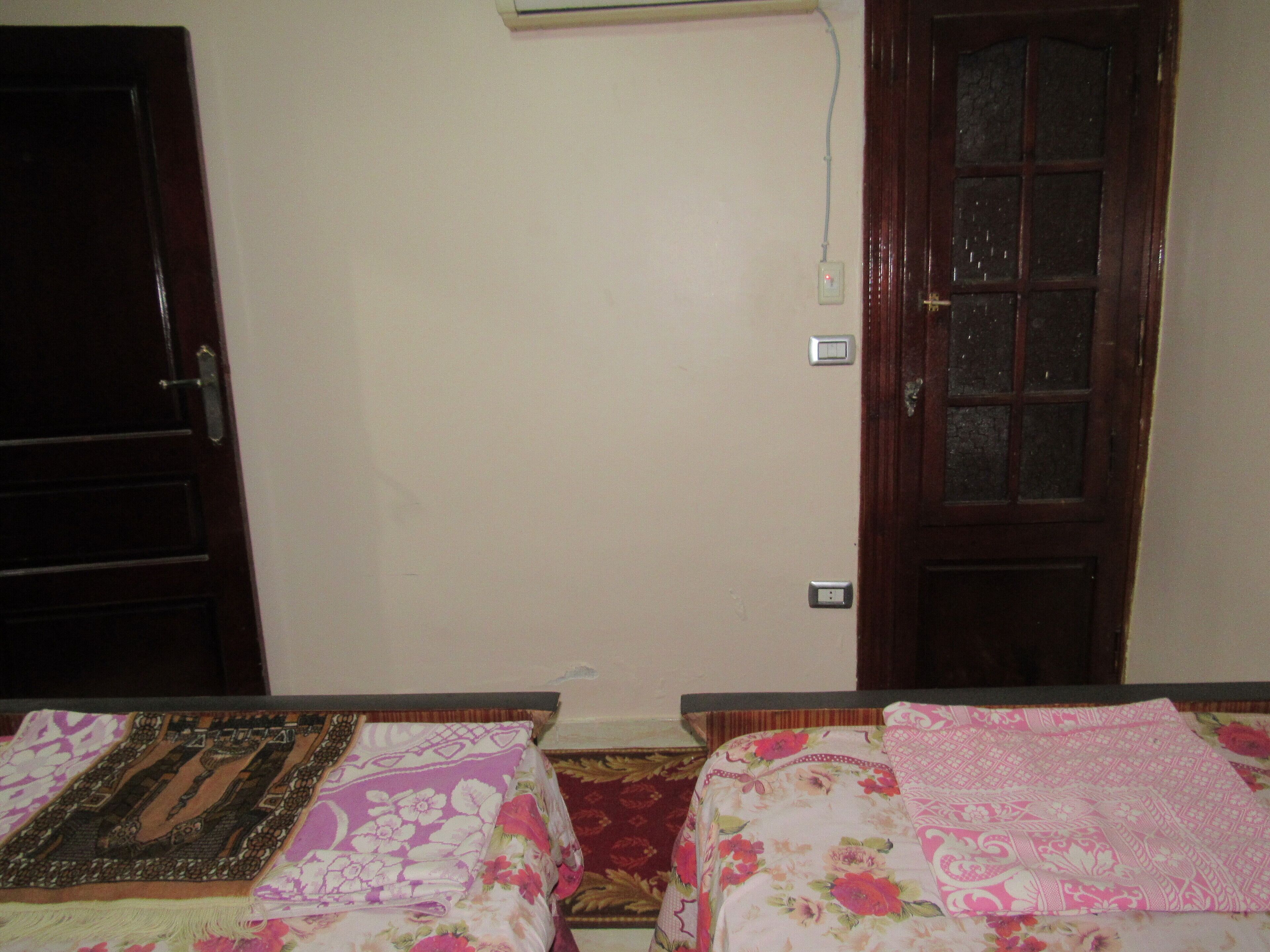 Une chambre avec deux lits, une porte en bois et une prise de courant au mur.