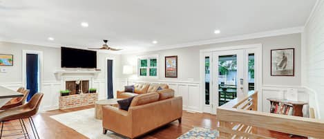 A spacious living room with a fireplace, leather sofa, and a dining area with a wooden table and chairs.
