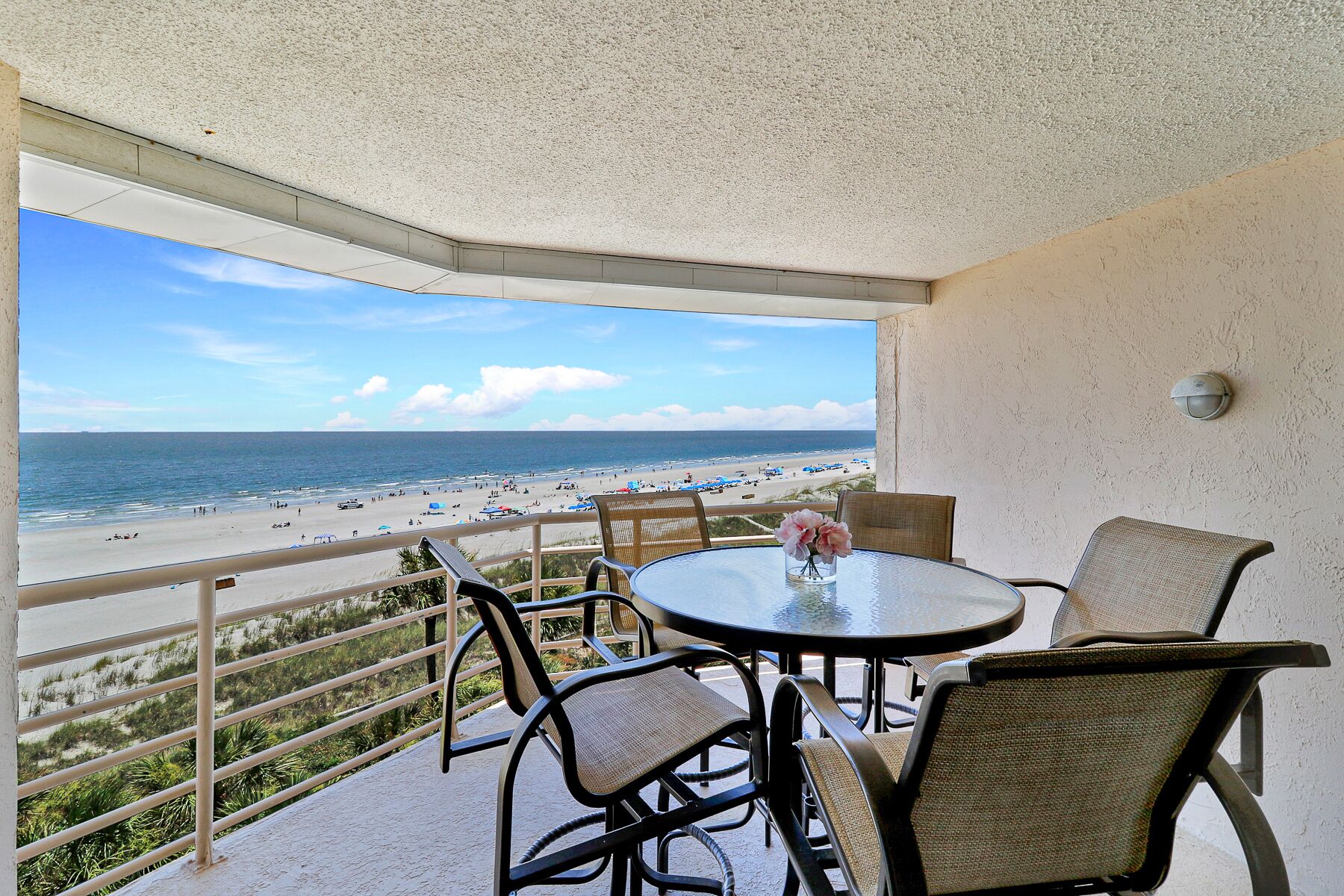 A balcony with a view of a beach, furnished with wicker chairs and a table.