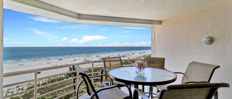 A balcony with a view of a beach, furnished with wicker chairs and a table.