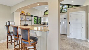 A kitchen with a central island, bar stools, and a white door. - Spacious 3-story home w/ stunning golf & lagoon views and large private pool (Hilton Head Island)