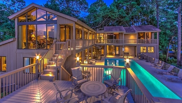 A multi-story wooden house with a swimming pool, outdoor seating, and a staircase leading to the upper levels. - Spacious 3-story home w/ stunning golf & lagoon views and large private pool (Hilton Head Island)