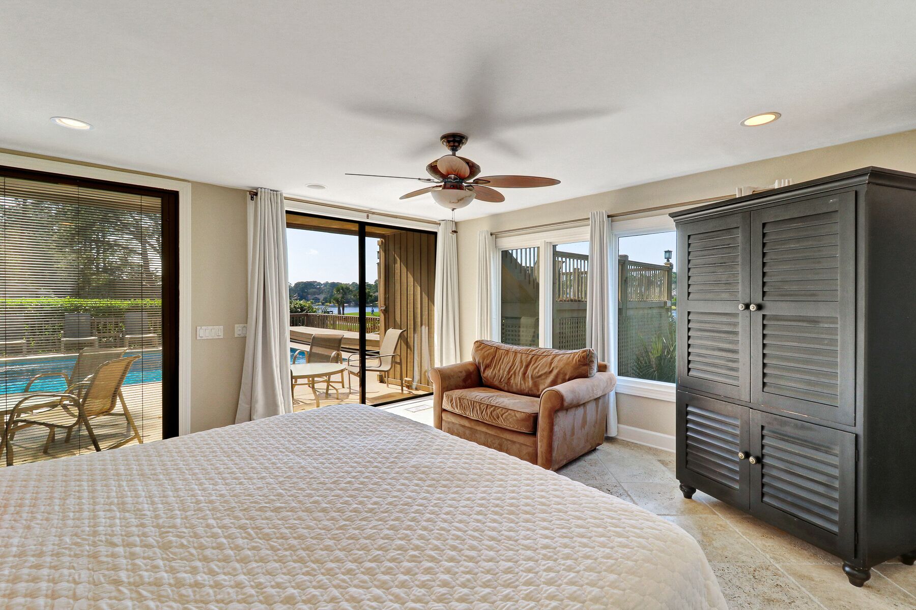 A bedroom with a large bed, a ceiling fan, a view of a pool, and a sliding glass door leading to an outdoor patio.