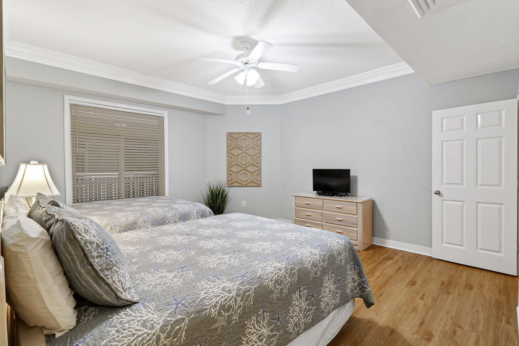 A bedroom with two beds, a ceiling fan, a TV on a dresser, and a door.