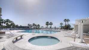 Un área de piscina con sillones reclinables, un jacuzzi y palmeras.