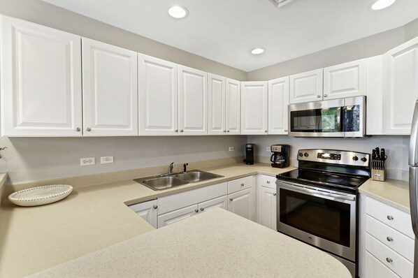 A modern kitchen with white cabinets, stainless steel appliances, and a beige countertop. - Oceanfront complex with pool & spa, only steps from beach & Coligny Plaza (Hilton Head Island)