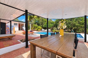 An outdoor patio with a wooden table and chairs, a pool, and a covered area with a view of the pool and greenery. - Unique experience in the nature of Aruba #1 (Paradera)
