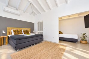 A modern bedroom with a large bed, bedside tables, a plant, and a view into another room. - Unique experience in the nature of Aruba #1 (Paradera)