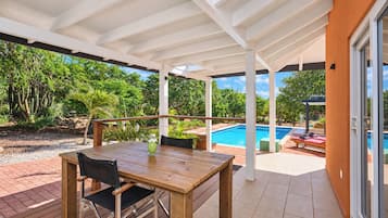 Une terrasse extérieure avec une table et des chaises en bois, une piscine et une végétation luxuriante.