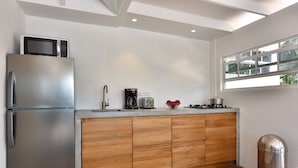 A compact kitchen with a stainless steel refrigerator, a wooden cabinet, a coffee maker, and a window providing natural light.